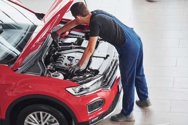 Widok z góry na pracownika płci męskiej w mundurze, który naprawia czerwony samochód