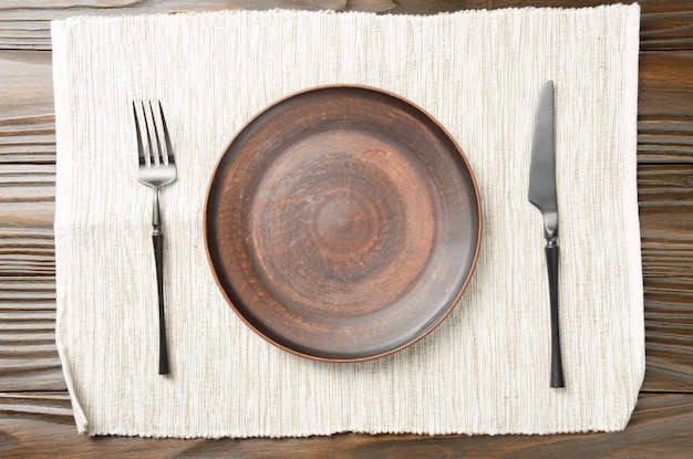 Widok z góry na pusty gliniany talerzyk i widelec na bok na szarej serwetce na brązowym drewnianym stole kuchennym