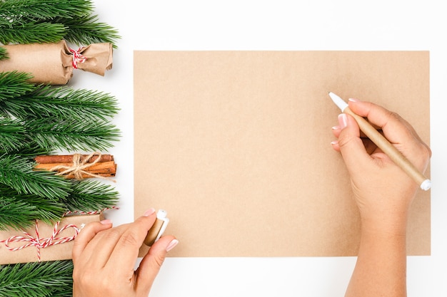 Widok z góry na ręce kobiety piszące noworoczną listę życzeń na papierze rzemieślniczym z ramą wykonaną z choinki ...