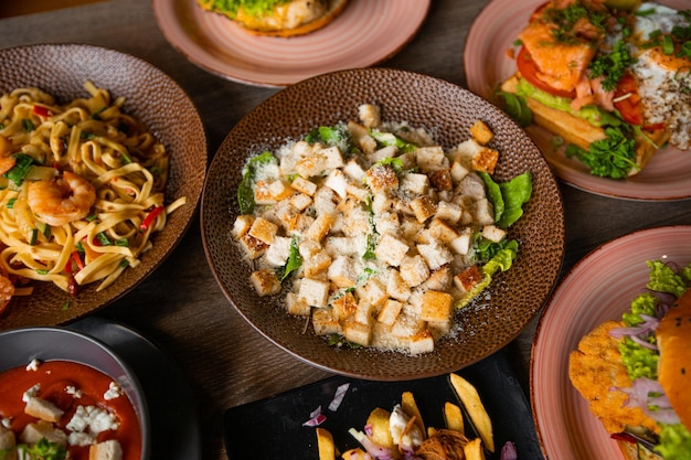 Widok z góry na smaczne jedzenie na talerzach na drewnianym stole w kawiarni restauracji Makaron z krewetkami Sałatka Cezar z sałatą