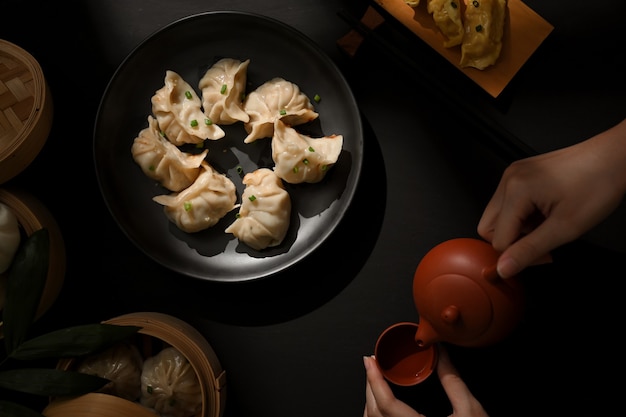 Widok z góry na stół z pierożkami Dimsum i kobiecą ręką z dzbankiem do herbaty w chińskiej restauracji