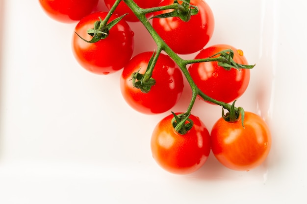 Widok z góry na świeże smaczne pomidory na zielonej gałęzi leżące na białym talerzu i wyglądające czysto