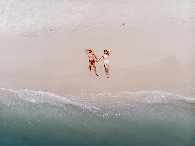 Widok z góry na szczęśliwą opiekuńczą parę w strojach kąpielowych leżącą na gorącym piasku plaży i opalającą się, trzymającą się za ręce pod promieniami palącego słońca. Pojęcie wspólnoty.