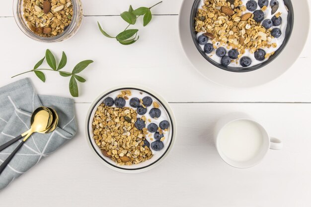 Widok z góry na trzy miski pieczonej muesli i świeżego mleka, jagód i orzechów. pyszne, zdrowe śniadanie. białe drewniane tło.