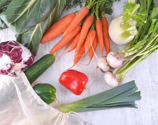 Widok z góry na warzywa w torbie wielokrotnego użytku wśród innych świeżych warzyw na białym stole