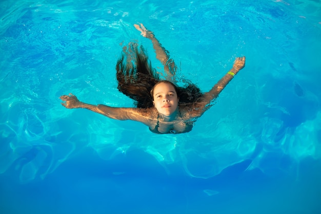 Widok z góry nastolatka dziewczyna pływa w basenie w ciepłej, czystej, błękitnej wodzie w słoneczne lato