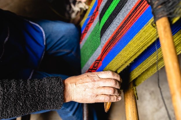 widok z góry nierozpoznawalne ręce starszej kobiety za pomocą domowego krosna rzemieślniczego do tkania kolorowej wełny
