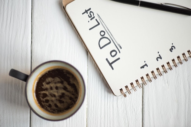 Widok z góry notebooka z napisem do listy i długopisem z filiżanką kawy na drewnianym tle