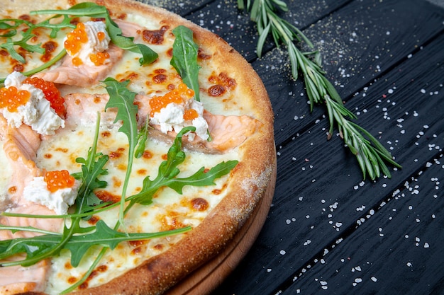 Widok z góry pizza z łososiem, rukolą, czerwonym kawiorem, serem na ciemnym drewnianym tle z odbitkowym sapce. Włoska pizza z owocami morza. Tło żywności Smaczna pizza domowej kuchni włoskiej
