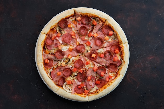 Widok z góry pizzy z szynką, bekonem, kiełbasą, pomidorem i pieczarkami