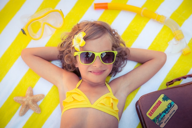 widok z góry portret dziewczyny w żółtych okularach przeciwsłonecznych i leżącej na ręczniku plażowym w paski