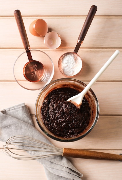 Widok z góry przygotowanie do pieczenia, ciasto mieszane z czekoladą na jasnej misce z białą szpatułką. robienie ciastek brownie lub babeczek czekoladowych