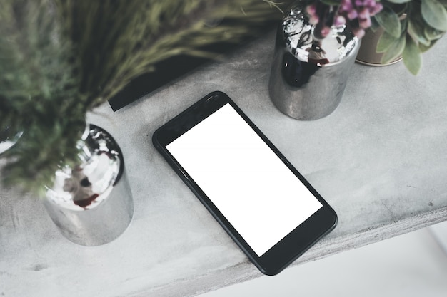 Zdjęcie widok z góry pusty biały ekran mobilny na betonowym stole z rośliną w wazonie