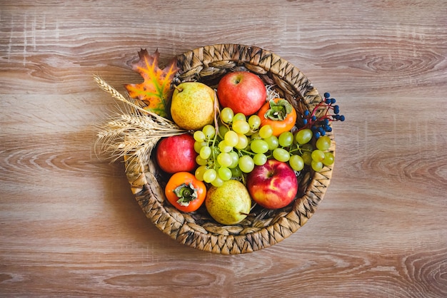 Zdjęcie widok z góry różnych kolorowych jesiennych owoców w wiklinowym koszu na drewnianym stole.