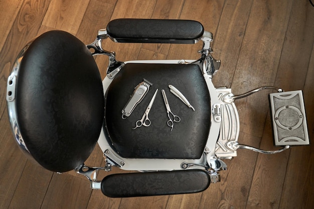 Widok z góry różnych narzędzi fryzjerskich na czarnym skórzanym krześle na drewnianej podłodze w salonie fryzjerskim