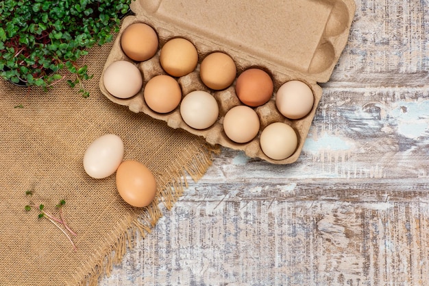 Widok z góry surowych jaj kurzych w pudełku na jajka na drewnianym tle z burlabem i mikro zieleniną