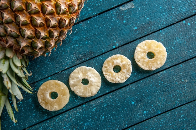 Zdjęcie widok z góry świeży ananas układający suszone pierścienie ananasa na niebieskim drewnianym tle