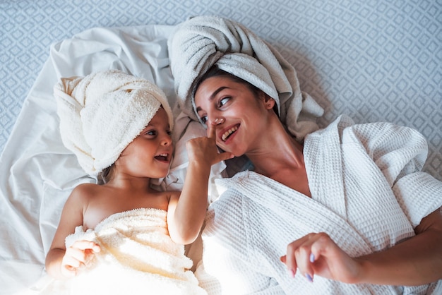 Widok z góry. Używając kremu. Młoda matka z córką mają dzień urody w pomieszczeniu w białym pokoju.