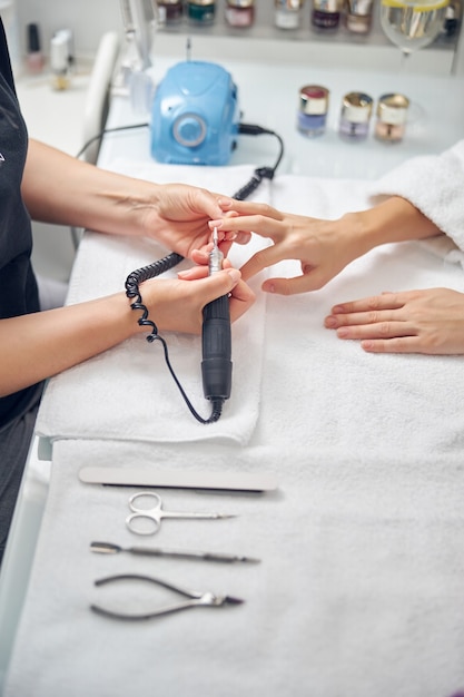 Widok z góry z bliska kobiecych rąk w pobliżu instrumentów podczas procedury manicure sprzętowego w salonie
