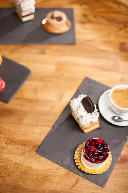 Widok z góry zdjęcie ciasta z pysznym ciastkiem w pobliżu różnych mini ciastek na drewnianym stole w kawiarni. Pyszne ciasto z pysznymi owocami na wierzchu i kremem do kawy.