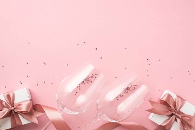 Widok z góry zdjęcie dekoracji walentynkowych błyszczące cekiny dwa kieliszki różowa satynowa wstążka i białe pudełka na prezenty z kokardkami na izolowanym pastelowym różowym tle z copyspace