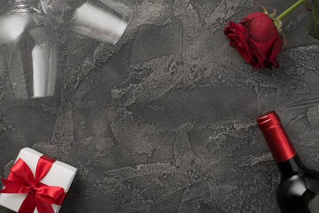 Widok z góry zdjęcie dekoracji walentynkowych dwa kieliszki butelka wina białe pudełko upominkowe z czerwoną kokardą i czerwoną różą na izolowanym teksturowanym ciemnoszarym betonowym tle z copyspace pośrodku