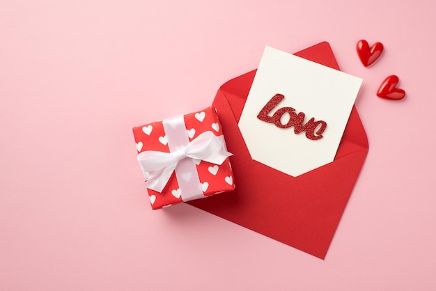 Widok z góry zdjęcie dekoracji walentynkowych małe serce pudełko upominkowe w papierze do pakowania z wzorem serc otwórz czerwoną kopertę z napisem karty miłość na białym tle pastelowe różowe tło z copyspace