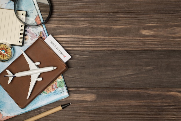 Widok z góry zdjęcie mapy lupy kompas notatnik pióro i model samolotu na skórzanej okładce paszportu z testem covid na na białym tle drewniany stół z copyspace