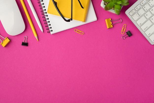 Widok z góry zdjęcie miejsca pracy z notatnikami kwiat klawiatura mysz żółte klipy kancelarii segregatory długopis i ołówek na na białym tle różowym z copyspace