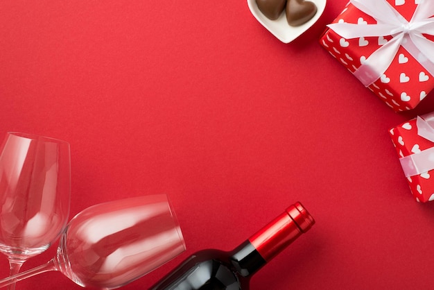 Widok z góry zdjęcie pudełek prezentowych w czerwonym papierze pakowym z wzorem serc i kokardek dwa kieliszki do wina spodek w kształcie serca z cukierkami i butelką wina na odizolowanym czerwonym tle z copyspace