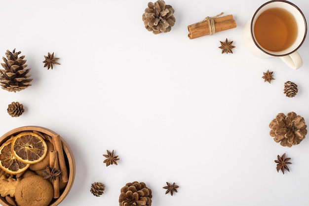 Widok z góry zdjęcie szyszek sosnowych w kompozycji zimowej filiżanka anyżu herbaty i drewniana miska z ciasteczkami cynamonu i suszonymi plasterkami cytryny na na białym tle z pustą przestrzenią pośrodku