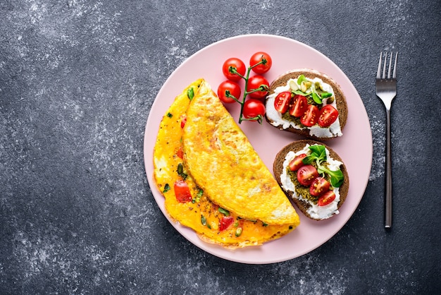 Widok z góry zdrowe Śniadanie składające się z omletu jajecznego, pełnoziarnistych tostów z twarogiem, pesto i pomidorkami koktajlowymi na różowym talerzu na czarnym kamiennym tle z kopią miejsca.