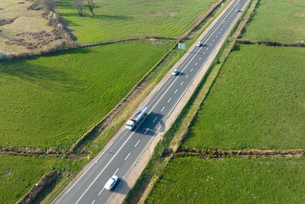 Widok z lotu ptaka drogi międzymiastowej między zielonymi polami rolnymi z szybkimi samochodami Widok z góry z drona ruchu na autostradzie