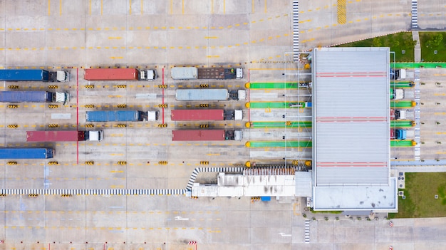 Widok z lotu ptaka dużych ciężarówek kontenerowych wchodzących z kontenerem towarów przez główną bramę wjazdową do portu przemysłowego.
