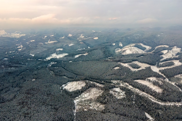 Widok z lotu ptaka jałowy zimowy krajobraz z górskimi wzgórzami pokrytymi wiecznie zielonym lasem sosnowym po obfitych opadach śniegu na zimny spokojny wieczór.