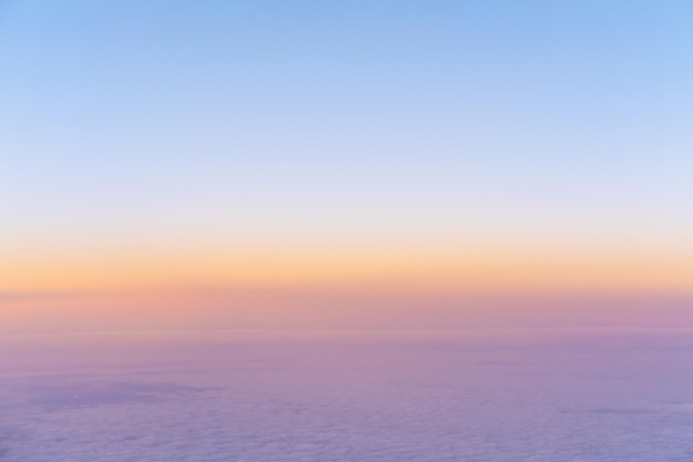 Widok z lotu ptaka jasnożółtego zachodu słońca nad różowymi fioletowymi gęstymi chmurami z błękitnym niebem nad głową z góry z samolotu