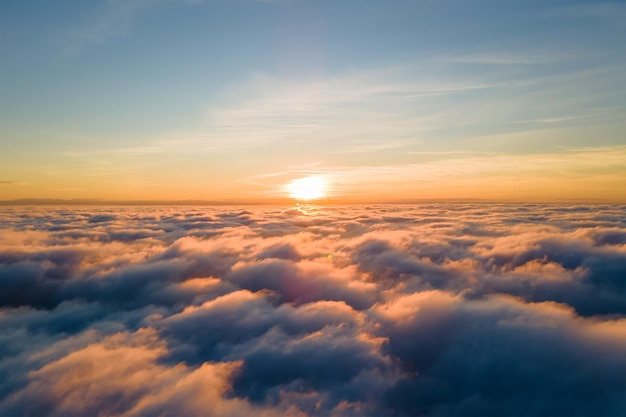 Widok z lotu ptaka jasnożółty zachód słońca nad białymi gęstymi chmurami z błękitnym niebem nad głową.