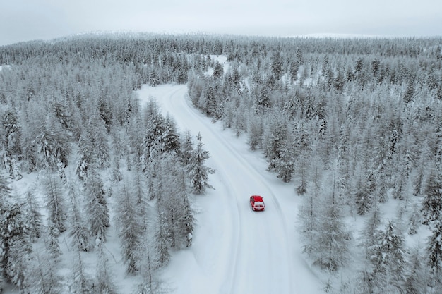 Widok z lotu ptaka na czerwony samochód jadący przez zaśnieżony las w Laponii, Finlandia