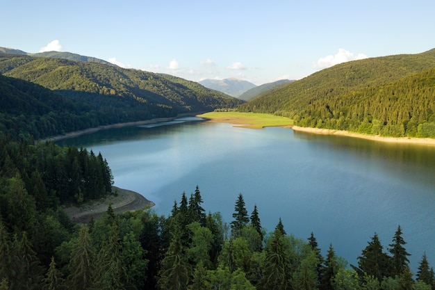 Widok z lotu ptaka na duże jezioro z czystą, błękitną wodą między wysokimi wzgórzami pokrytymi gęstym, wiecznie zielonym lasem.