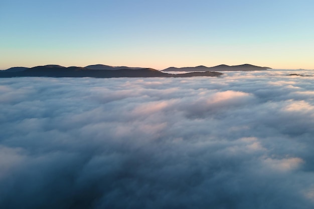 Widok z lotu ptaka na kolorowy wschód słońca nad białą gęstą mgłą z odległymi ciemnymi sylwetkami górskich wzgórz na horyzoncie