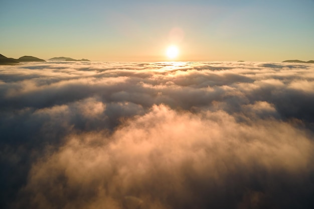 Widok z lotu ptaka na kolorowy wschód słońca nad białą gęstą mgłą z odległymi ciemnymi sylwetkami górskich wzgórz na horyzoncie