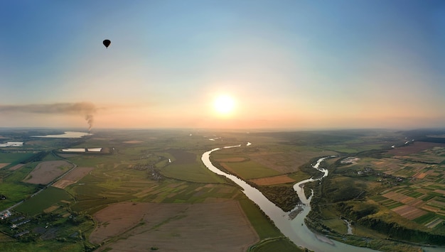 Widok z lotu ptaka na mały balon na gorące powietrze lecący nad wiejską okolicą o zachodzie słońca