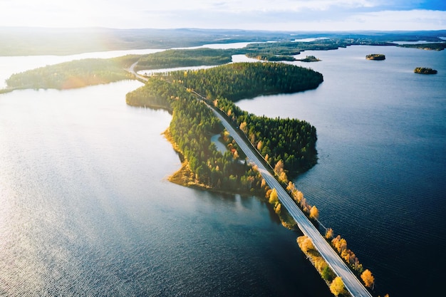 Widok z lotu ptaka na most nad niebieskimi jeziorami ze światłem słonecznym w kolorowym jesiennym lesie w Finlandii Laponia