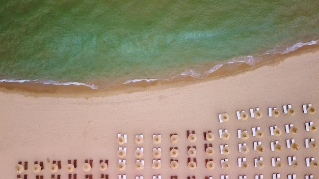 Widok z lotu ptaka na niesamowitą pustą piaszczystą plażę ze słomianymi parasolami i turkusową czystą wodą