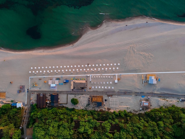 Widok z lotu ptaka na piaszczystą plażę z parasolami, morze i las nad Morzem Bałtyckim w Yantarnym o zachodzie słońca