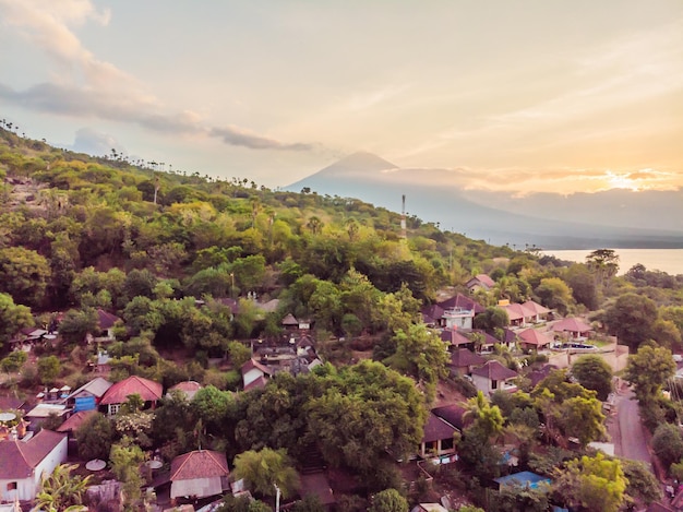 Widok z lotu ptaka na plażę Amed na Bali, Indonezja Tradycyjne łodzie rybackie zwane jukung na czarnej, piaszczystej plaży i wulkan Mount Agung w tle częściowo zasłonięty chmurami