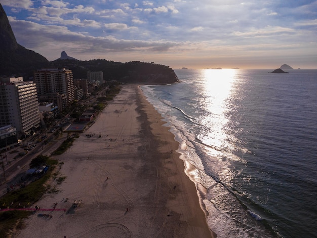 Widok z lotu ptaka na plażę Barra da Tijuca, raj w zachodniej części Rio de Janeiro, Brazylia. Wokół duże wzgórza, takie jak Pedra da GÃƒvea. Słoneczny dzień z chmurami o świcie. Zielonkawe morze. Zdjęcie z drona.