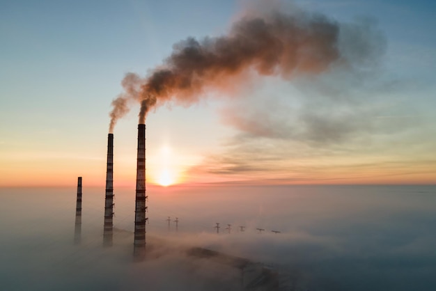 Widok z lotu ptaka na wysokie rury elektrowni węglowej z czarnym dymem w górę zanieczyszczającej atmosfery o zachodzie słońca