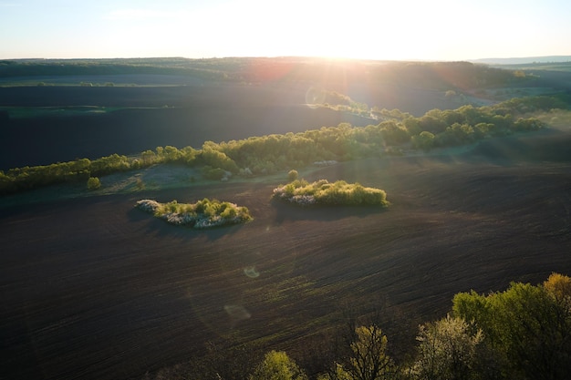 Widok z lotu ptaka na zaorane pola uprawne z żyzną glebą uprawną przygotowaną do sadzenia roślin między zielonymi lasami na wiosnę