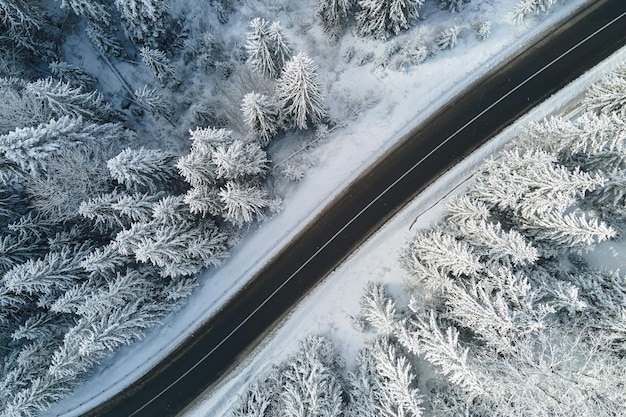 Widok z lotu ptaka na zimowy krajobraz z pokrytymi śniegiem lasami górskimi i krętą leśną śliską drogą.